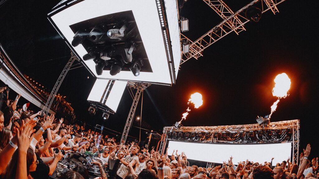 Menschenmenge bei einem nächtlichen Musikfestival mit Feuereffekten.