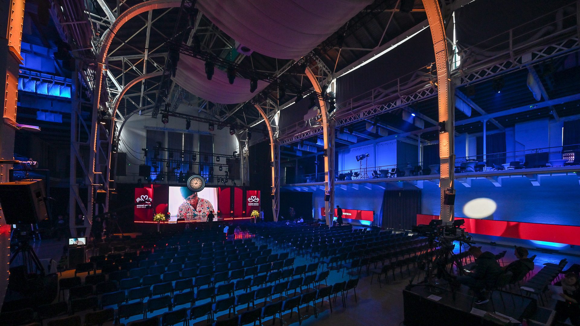 Großer beleuchteter Konferenzraum mit Leinwand auf der Bühne.