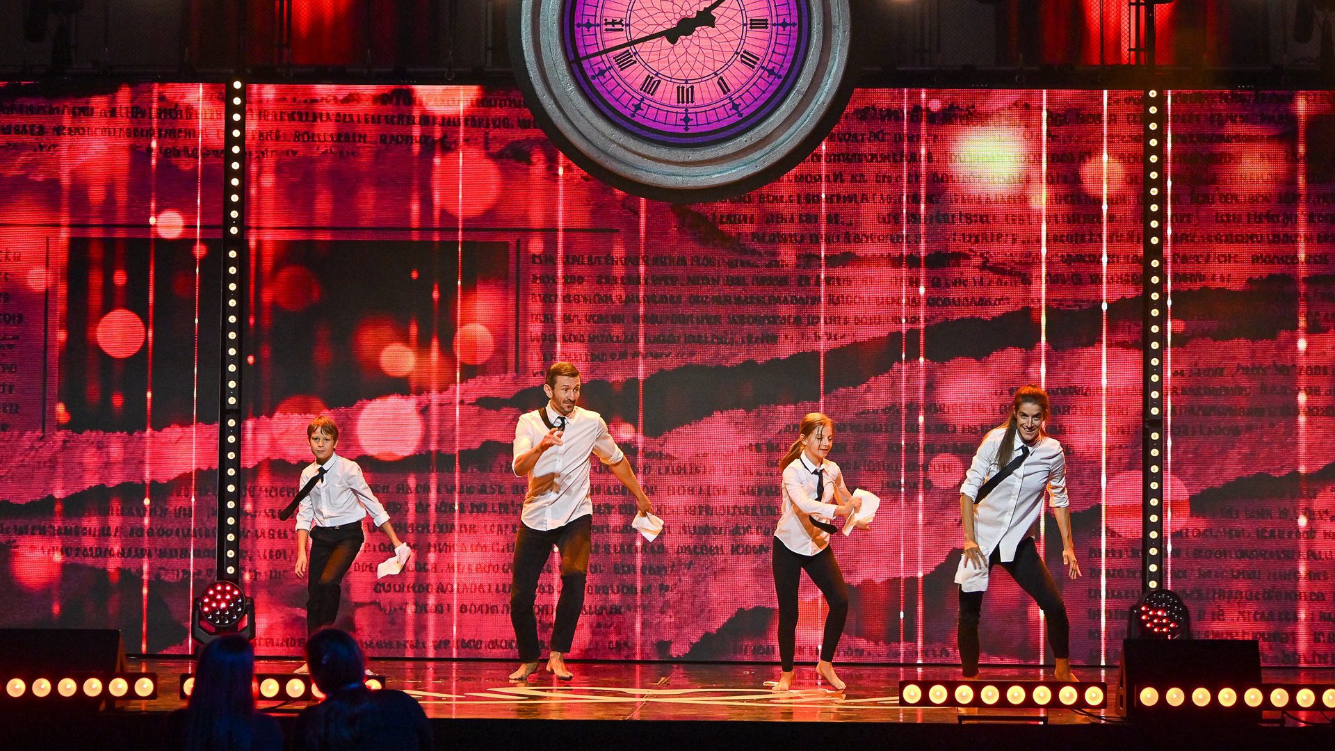 Die Gruppe betritt die Bühne mit einer farbenfrohen Kulisse.