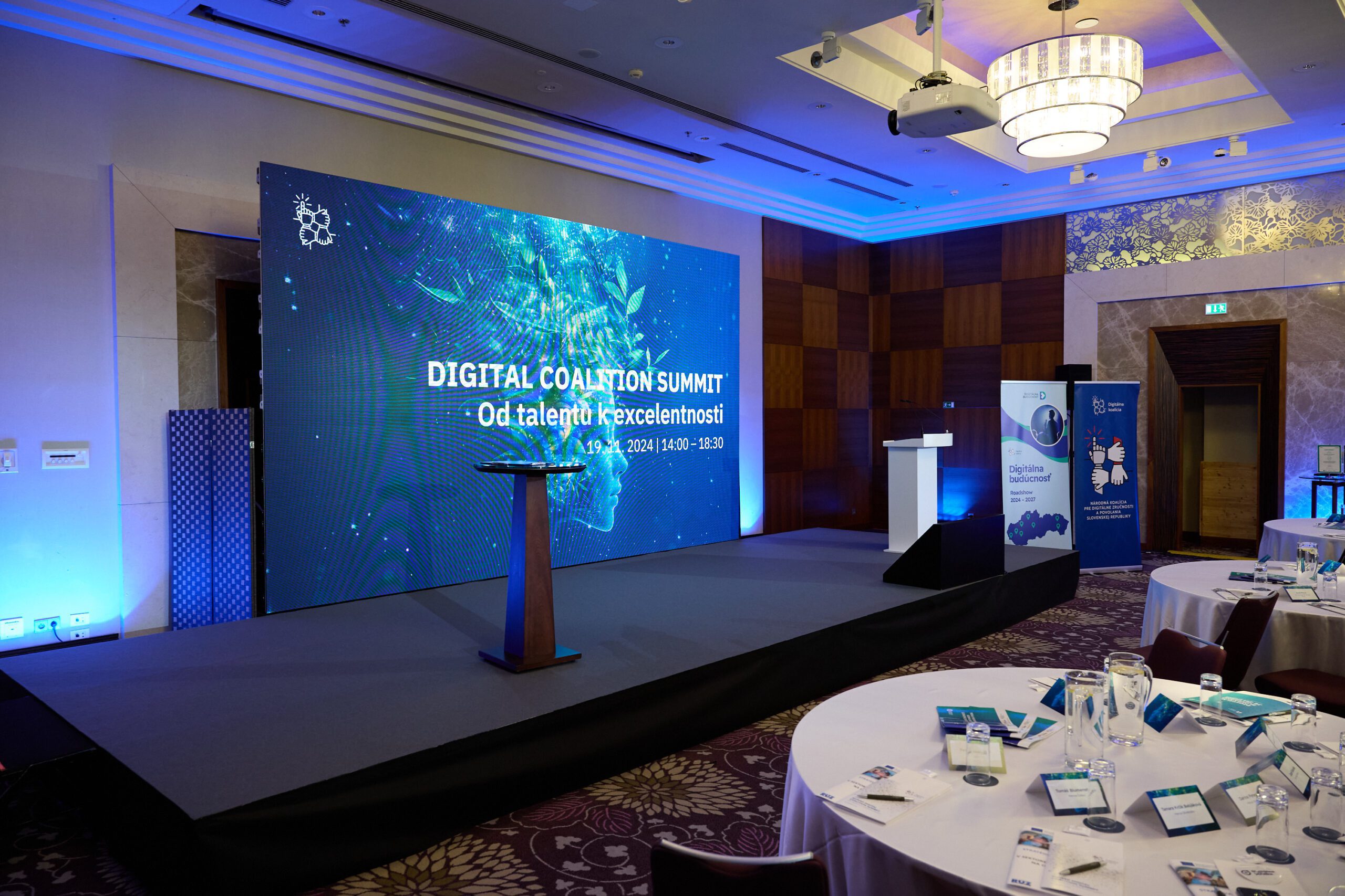 Der Redner steht auf der Bühne und präsentiert vor einem großen LED-Bildschirm mit dem Thema der digitalen Zukunft.