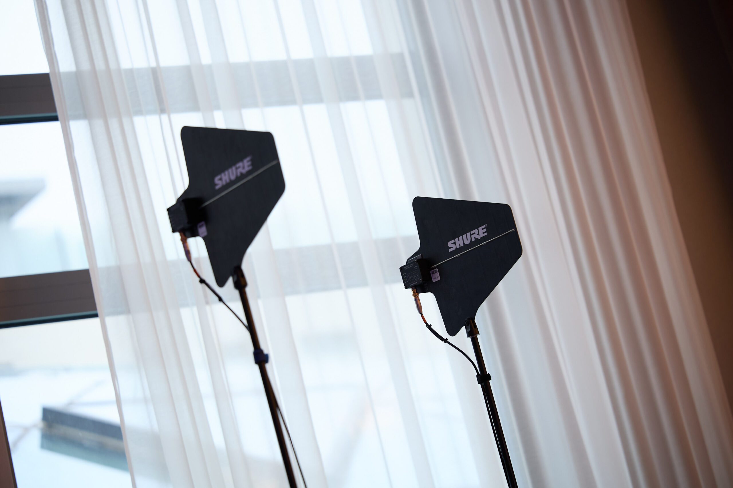 Zwei drahtlose Mikrofonantennen von Shure vor dem weißen Vorhang.