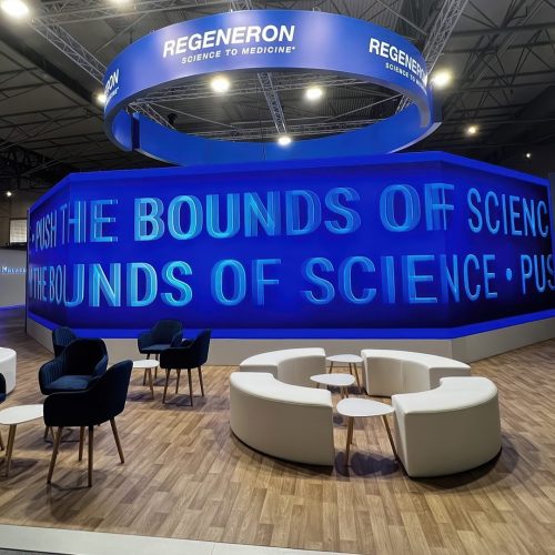 Messestand mit Sitzgelegenheit und Bildschirmen.